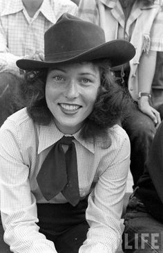 a woman wearing a hat and tie sitting on the ground with other people behind her