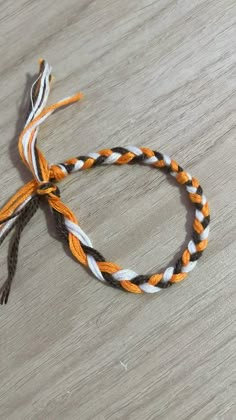 an orange, white and black braided bracelet on a wooden table with a knot