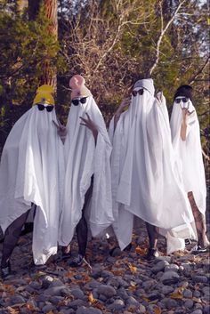 three people dressed in white robes and yellow hats are standing on rocks with trees in the background