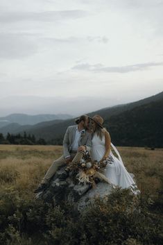 a bride and groom sitting on top of a rock in the middle of a field