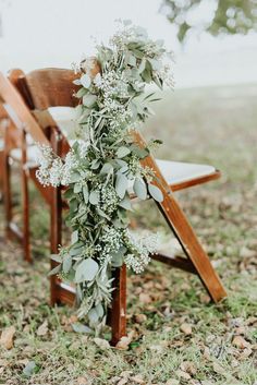 an arrangement of flowers and greenery on the back of a wooden chair at a wedding ceremony