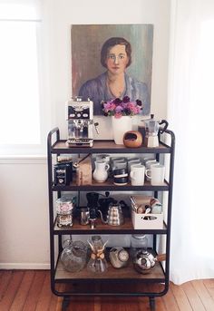 a shelf with coffee cups and other items on it in front of a painting by a window