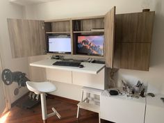 two computer monitors sitting on top of a desk next to a white chair and table