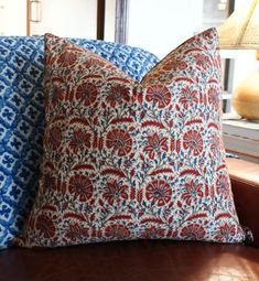 two blue and red pillows sitting on top of a brown leather couch next to a lamp