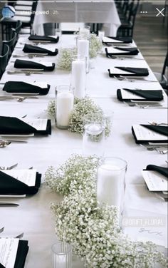 a long table is set with black and white place settings, silverware, and baby's breath flowers