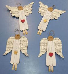 four angel ornaments made out of sheet music with hearts and gold stars on them, sitting on a blue surface