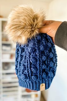 a person holding up a blue hat with a fur pom