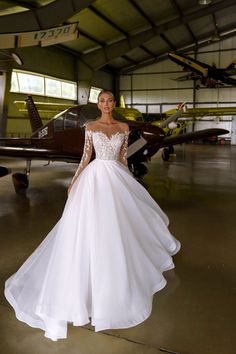 a woman standing in front of an airplane wearing a wedding dress with long sleeves and beading