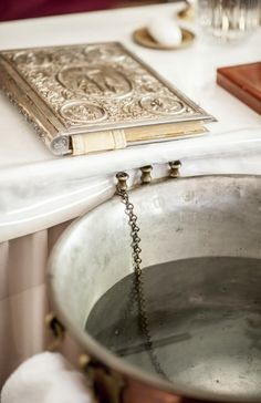 an old book is on the table next to a metal pan with a chain hanging from it