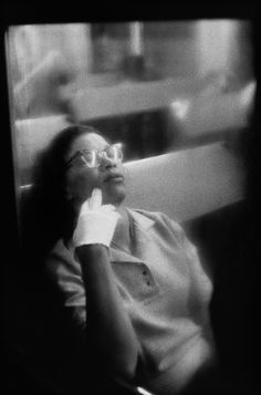 a black and white photo of a woman with glasses sitting in a chair looking off into the distance