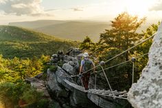 a man walking across a rope bridge on top of a mountain in the sun light