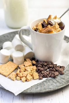 a cup filled with marshmallows, chocolate chips and graham crackers on a plate