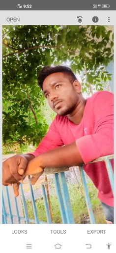 a man in pink shirt leaning on blue railing with trees behind him and the caption reads,