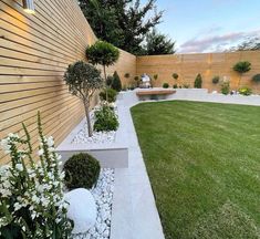 a garden with grass, rocks and plants next to a wooden fenced in area