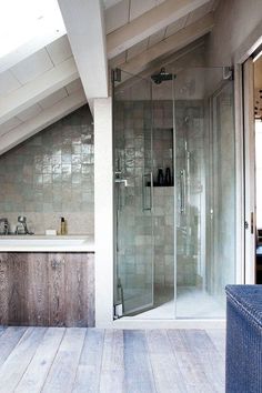 a bathroom with a walk in shower next to a white sink and wooden flooring