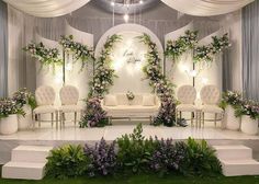 a stage set up for a wedding ceremony with flowers and greenery on the walls