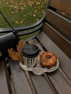 a cup of coffee sitting on top of a wooden bench next to a donut