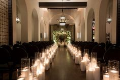 rows of lit candles are lined up along the wall in front of an arched doorway