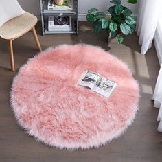 a pink round rug on top of a wooden floor next to a chair and potted plant