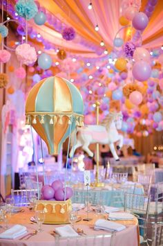 a table topped with lots of tables covered in pink and blue balloons next to a carousel