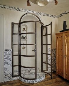 a bathroom with marble walls and flooring has an arched shower enclosure in the corner