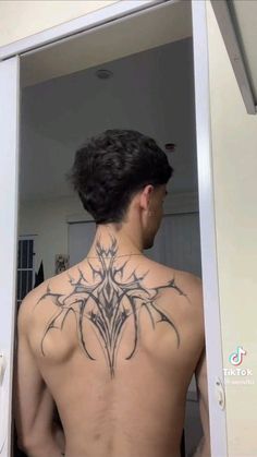 a man with a tattoo on his back standing in front of a mirror and looking at himself