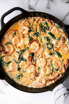 a skillet filled with shrimp and spinach on top of a marble countertop