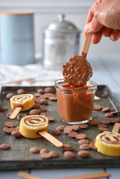 someone dipping chocolate into some kind of dessert on a cookie sheet with other treats around it