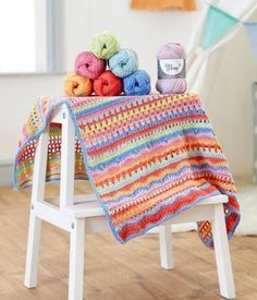 a crocheted blanket sitting on top of a wooden chair next to balls of yarn