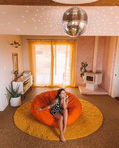 a woman sitting on an orange bean bag chair in a living room with a disco ball hanging from the ceiling