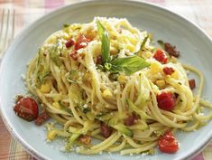 a white plate topped with pasta and vegetables on top of a checkered table cloth