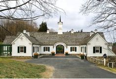 a large white house with green shutters on the front and side doors, surrounded by trees