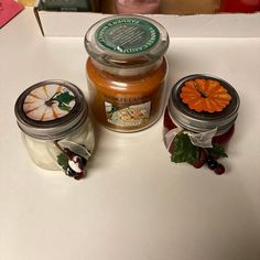 three jars of honey sit on a table next to each other, one with an orange flower