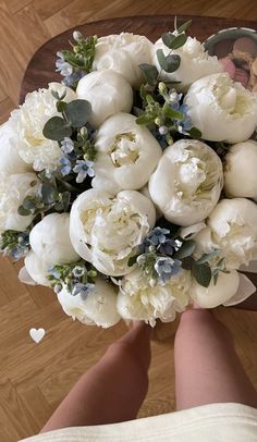 a bridal bouquet with white flowers and greenery in someone's hand on a wooden floor