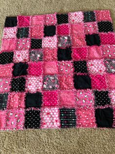 a pink and black patchwork quilt laying on the floor in front of a carpet