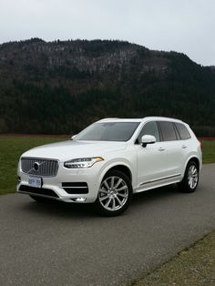 a white volvo suv parked on the side of a road in front of a mountain