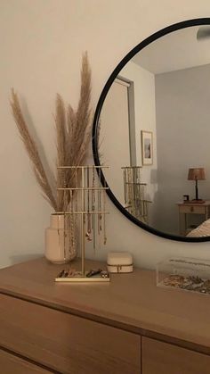 a round mirror is on the wall above a dresser with a vase and other items