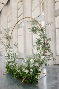 an arrangement of white flowers and greenery is arranged in a circular basket on the floor