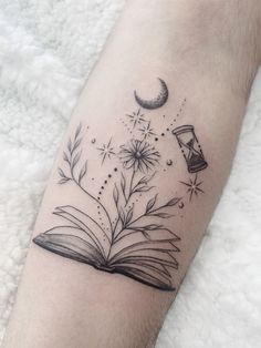 an open book tattoo on the arm with flowers and books flying in the sky above it