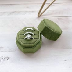 an engagement ring in a velvet box on a white wooden floor with a green cushion