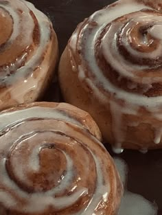 three cinnamon rolls sitting on top of a pan covered in icing