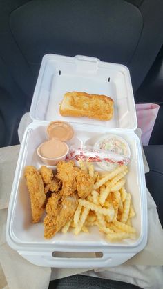 a plastic container filled with fried chicken and french fries next to dipping sauce in a cup