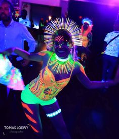 a woman in neon clothing dancing on a dance floor with other people behind her at a party