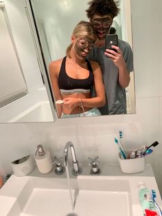 a man and woman standing in front of a bathroom mirror looking at their cell phones