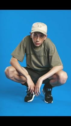 a young man sitting on the ground with his hands in his pockets and wearing a hat