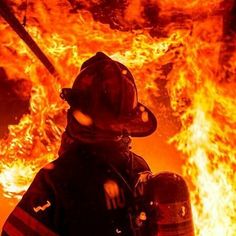 a firefighter standing in front of a large fire with his helmet on and arms crossed