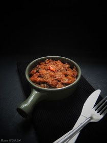 a bowl filled with meat next to a fork and knife on a black tablecloth