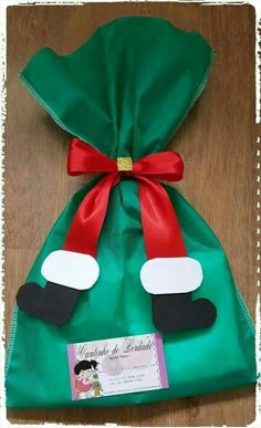 a green bag with red ribbon and santa's hat on it sitting on top of a wooden table