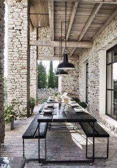 an outdoor dining area with wooden tables and benches, surrounded by stone walls and windows