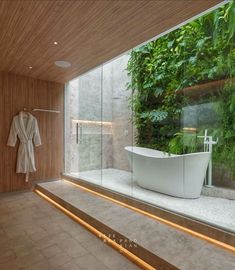 a bathroom with a bathtub and plants on the wall behind it, in front of a glass door